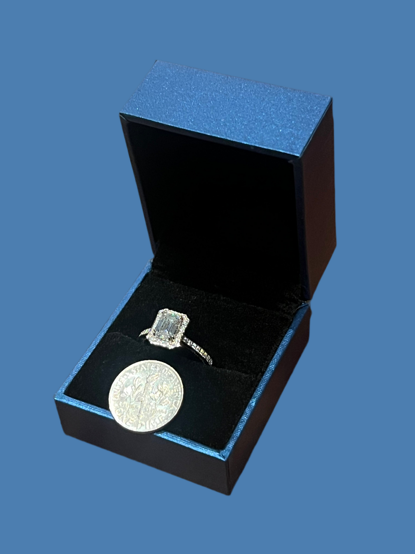 Emerald-cut moissanite engagement ring in blue box beside coin, ethical lab-made jewelry