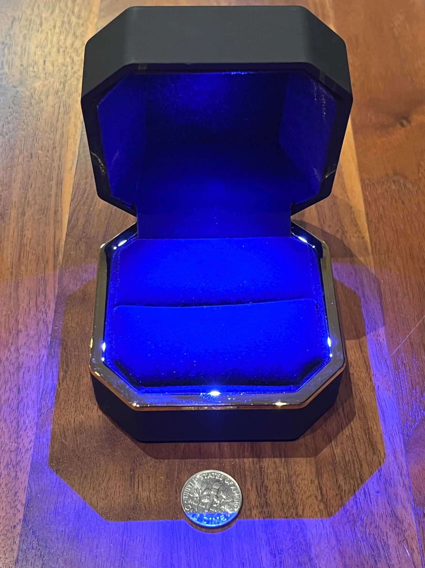 Empty moissanite ring box with blue LED light and coin on wooden table, Moissanright jewelry