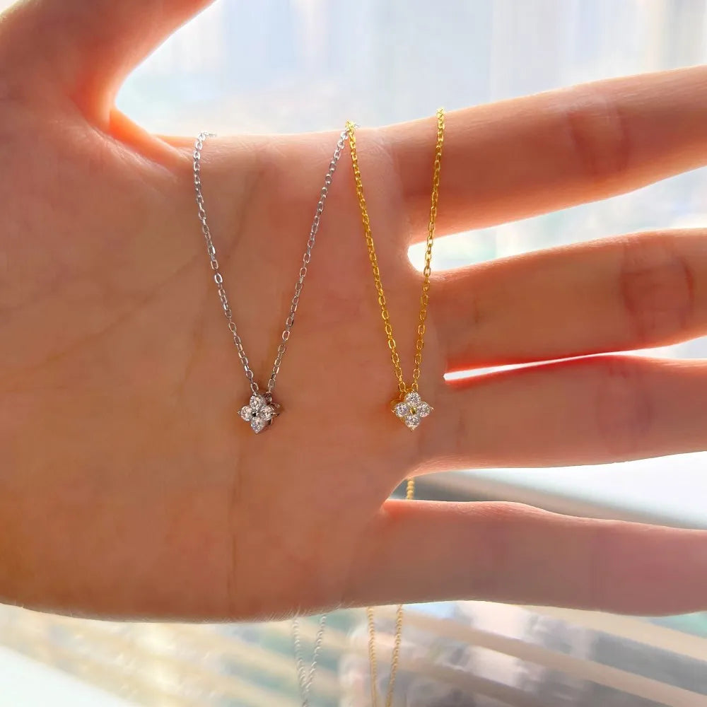 Hand displaying two moissanite pendant necklaces, one silver and one gold, with lab-made stones