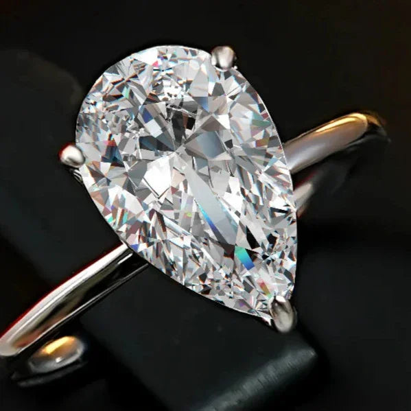 Pear-shaped moissanite engagement ring on silver band, sparkling on black background