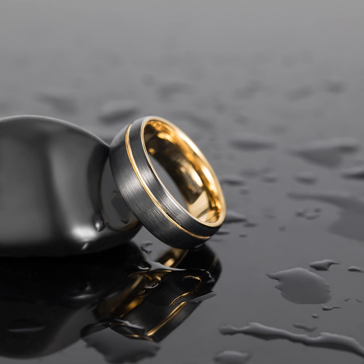 Brushed black and gold men's wedding band on wet reflective surface, Moissanright jewelry