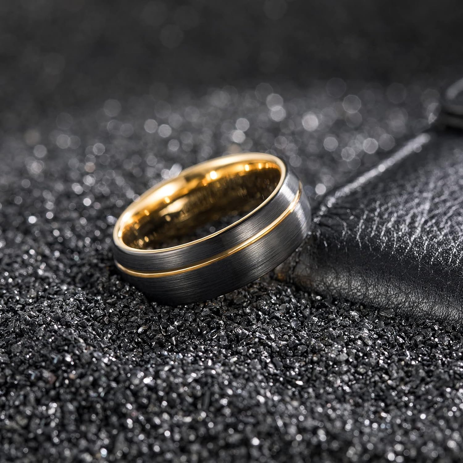 Brushed black and gold men's wedding band on glittery black background, modern jewelry design